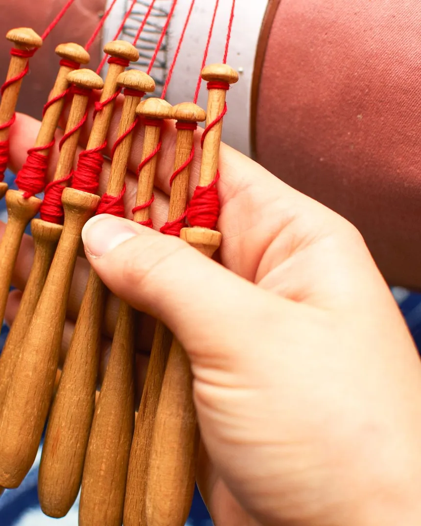 Detalle de bolillos de madera con el hilo rojo devanado en el cuello, sostenidos junto al mundillo